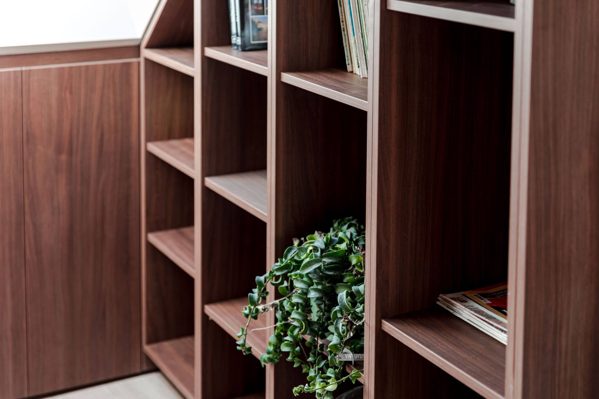 Boekenkast op maat in walnut die de schuine wand van een zolder volgt