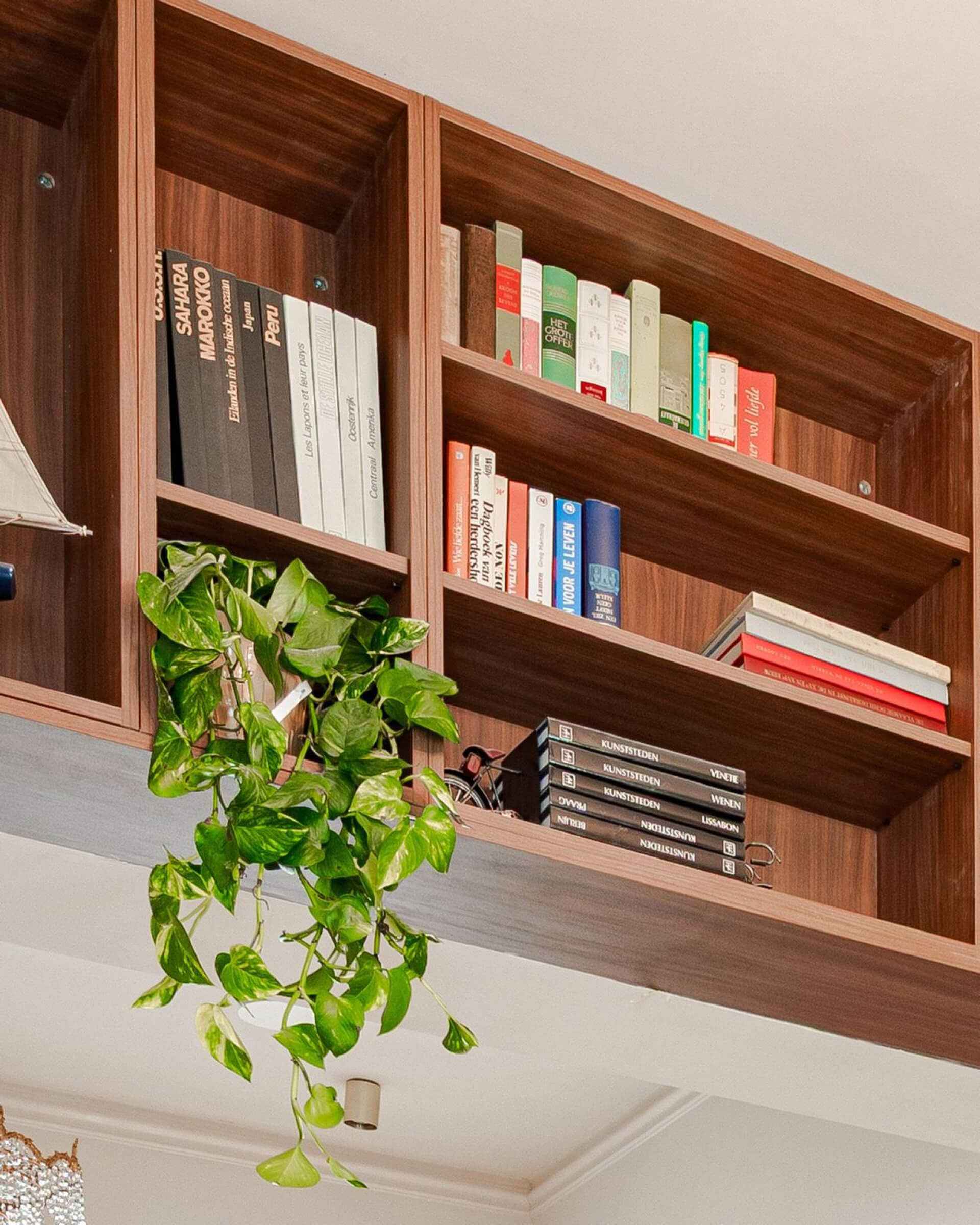 Open boekenkast op maat in walnut boven een doorgang, met boeken en een hangplant