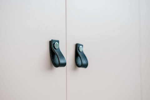 Gros plan d’un meuble blanc avec des poignées boucle en cuir noir.