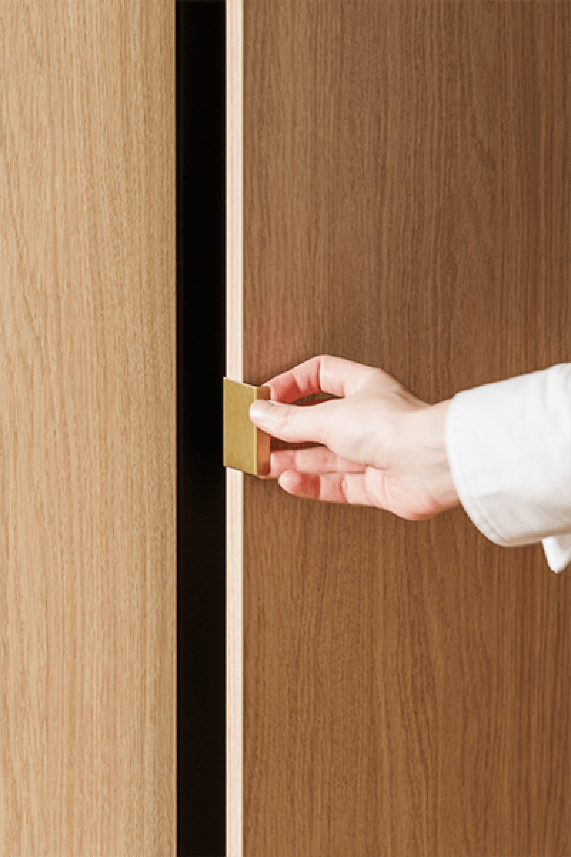 Detail shot van een mini pure messing handgreep op een maatkast in Atlas Oak. Rechts is er een hand die de deur van de kast opent.