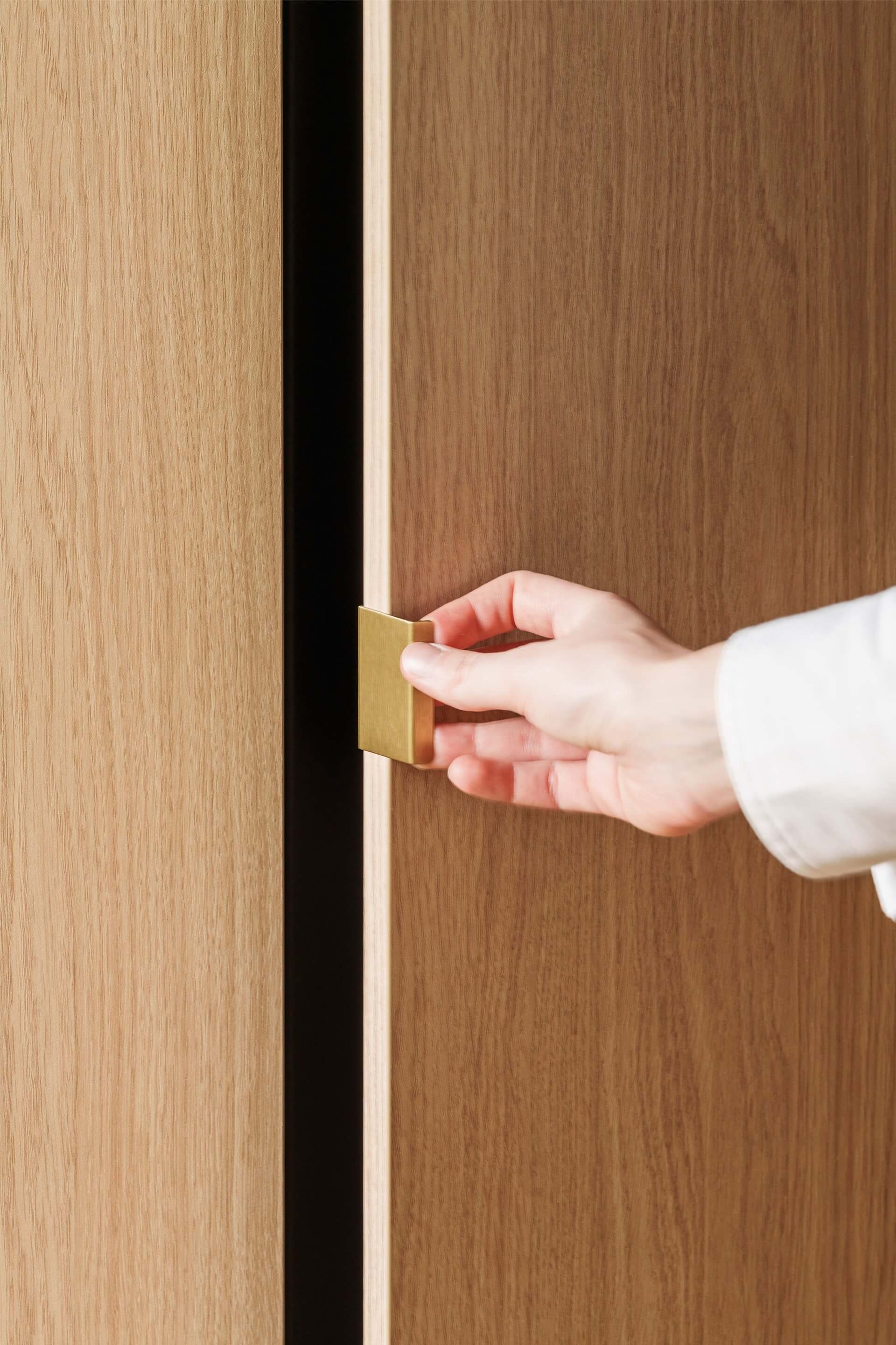 Detail shot van een mini pure messing handgreep op een maatkast in Atlas Oak. Rechts is er een hand die de deur van de kast opent.